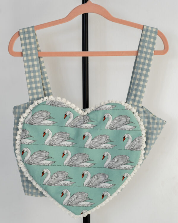 Delantero top de tirantes estilo corazón en verde agua con estampado de cisnes y cuadros vichy colgado en percha rosa