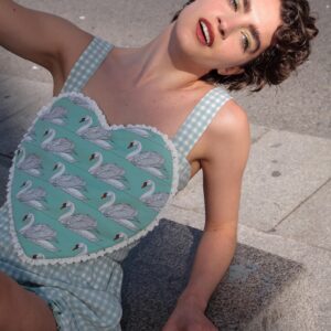 Modelo con top de tirantes setilo corazón en verde agua con estampado de cisnes y cuadros vichy, sonriendo al sol en una calle urbana