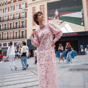 Modelo con vestido largo de encaje rosa, mangas abullonadas y detalles en vichy frente a Cines Callao en Madrid