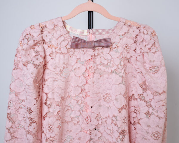 Detalle cuello con lazo de vestido largo de encaje rosa, mangas abullonadas y detalles en vichy