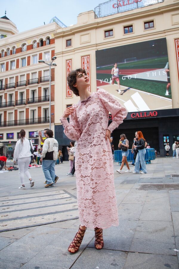 Modelo con vestido largo de encaje rosa, mangas abullonadas y detalles en vichy frente a Cines Callao en Madrid