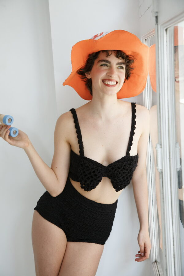 Modelo con conjunto de top y culote de punto negro con sombrero naranja y prismáticos en la mano