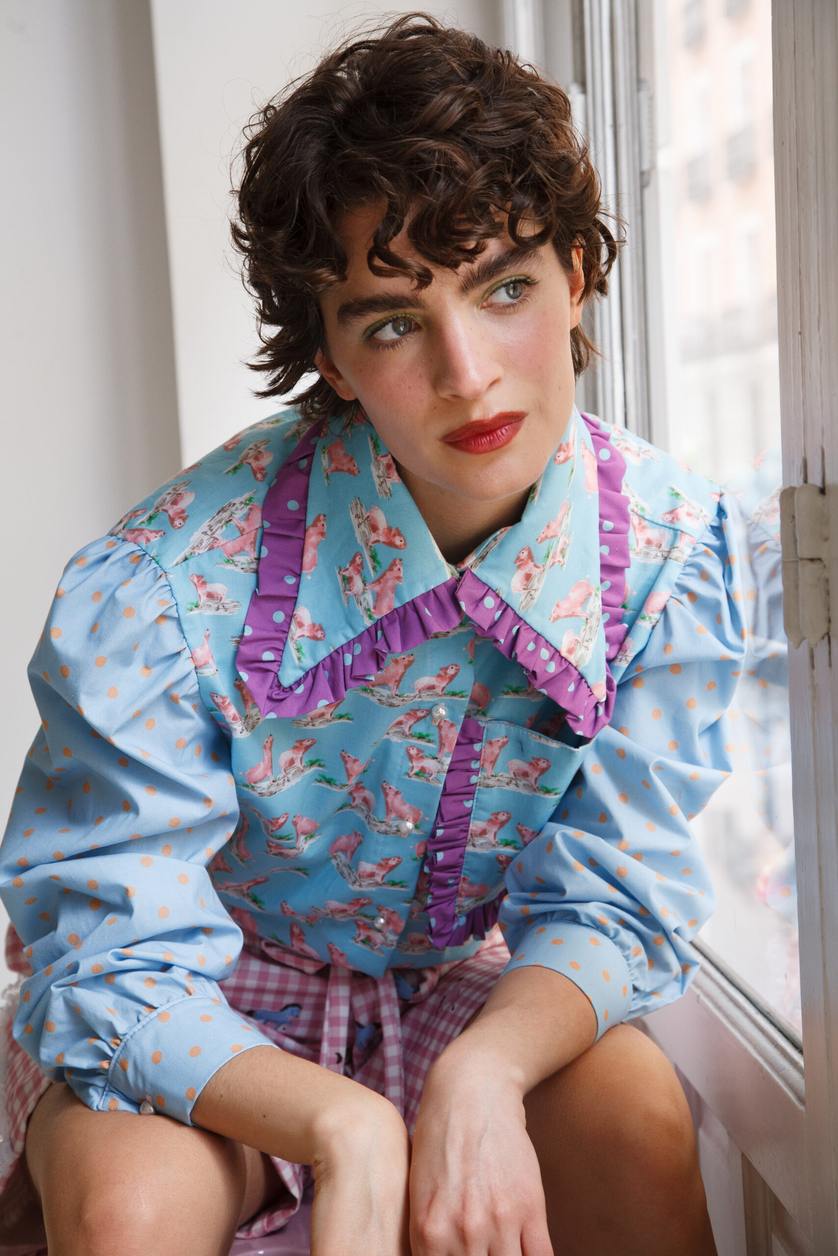 Persona vistiendo la camisa Lady Iris Pig, una prenda celeste con estampado de cerditos rosados, volantes lavanda y mangas con lunares