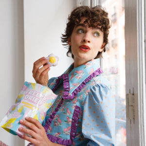 Persona vistiendo la camisa Lady Iris Pig, una prenda celeste con estampado de cerditos rosados, volantes lavanda y mangas con lunares